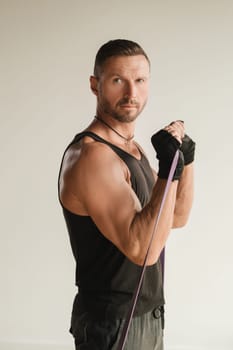 A man in black sportswear is engaged in strength fitness using a rubber loop indoors.