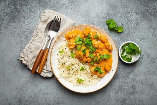 Traditional Indian dish chicken curry with basmati rice and fresh cilantro on rustic white plate on gray concrete table background from above. Indian dinner meal