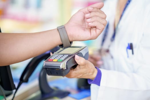 Unrecognizable man paying by smartwatch with dataphone in a pharmacy, attended by a female pharmacist holding the payment system.