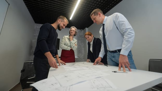 Four business people review and discuss blueprints. Designers engineers at a meeting