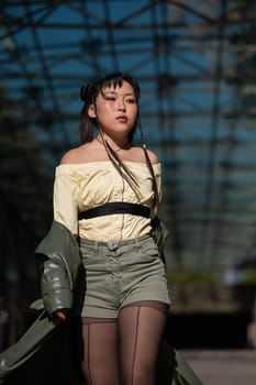 A beautiful Asian woman in shorts and a green leather coat comes out of the subway