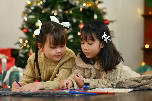 Two little girls making greeting card for New Year and Christmas while lying on floor in living room.