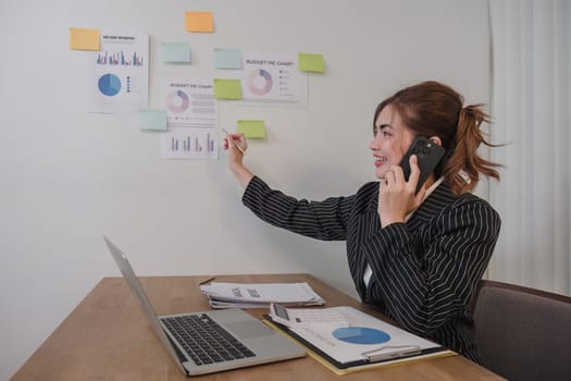 Asian businesswoman in a formal suit in the office is happy and cheerful while using a smartphone to work in her office..