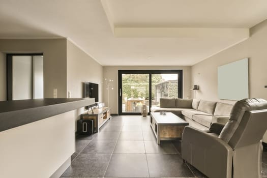 a living room with tile flooring and white walls, there is an open door leading to the patio area