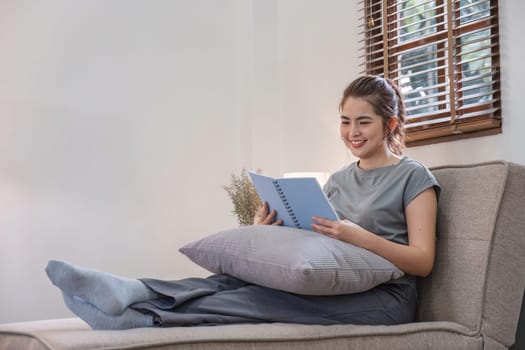 Happy young woman reading book on sofa at home. Lifestyle freelance relax in living room. Lifestyle Concept.