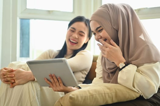 Two happy best friends laughing while watching funny videos on digital tablet.