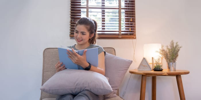 Happy young woman read book on sofa at home. Lifestyle freelance relax in living room. Lifestyle Concept.