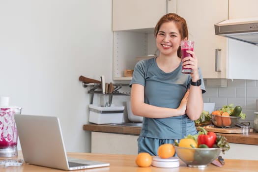 Beautiful young woman in exercise clothes having fun in a cute kitchen at home. Preparing a vegetarian fruit salad or a healthy smoothie..