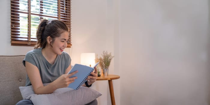 Happy young woman read book on sofa at home. Lifestyle freelance relax in living room. Lifestyle Concept.