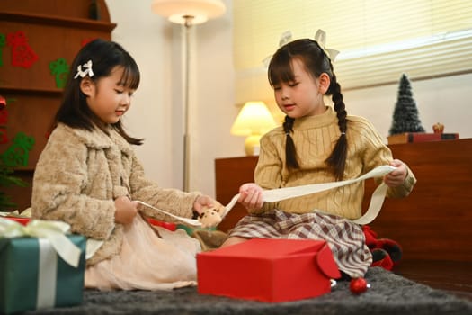 Surprised children opening Christmas gift in beautifully decorated living room and enjoying holiday season at home.