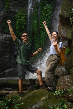 Happy young woman tourist with backpack enjoying tropical waterfall view. Travel and active life concept.