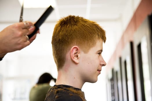 smiling young boy with red hair at the hairdresser