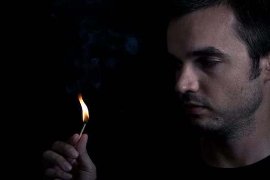 Dramatic portrait of man lighting safety match, over black background.