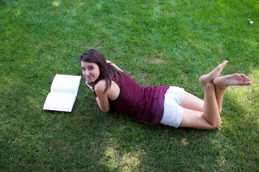 A pretty girl reads a book in her backyard.