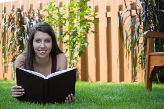 A pretty girl reads a book in her backyard.