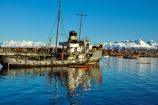 An old boat with Ushuaia and the mountains of Tierra del Fuego behind it.
