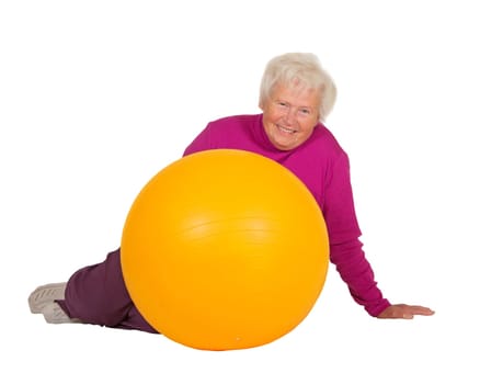 Healthy retired woman with a radiant smile full of vitality resting on the floor alongside her gym or pilates ball after a workout isolated on white