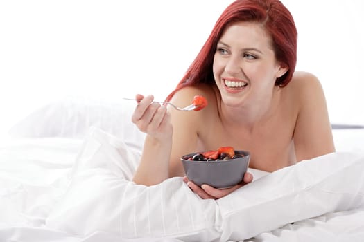 Attractive young woman on her bed at home eating fresh fruit for breakfast