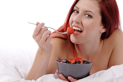 Attractive young woman on her bed at home eating fresh fruit for breakfast