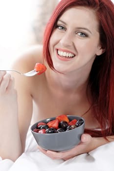 Attractive young woman on her bed at home eating fresh fruit for breakfast
