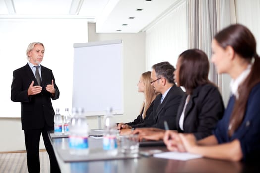 Mature male business executive training his associates during a meeting at office