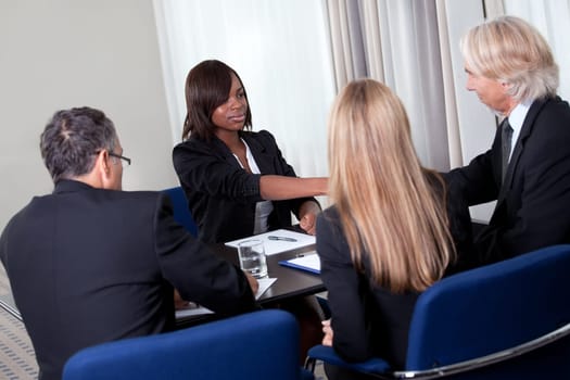 Mature group of business managers conducting job interview shaking hands with applicant at a table in meeting room