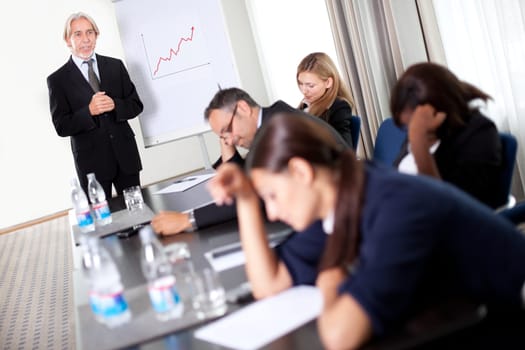 Businessman discussing sales targets at a meeting with his inattentive and sleepy team