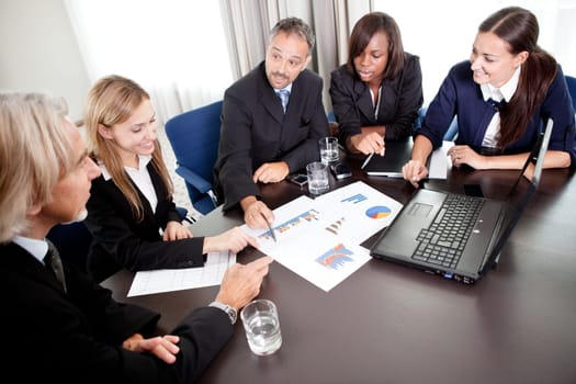 Young pretty females with mature business managers discussing targets at work on laptop