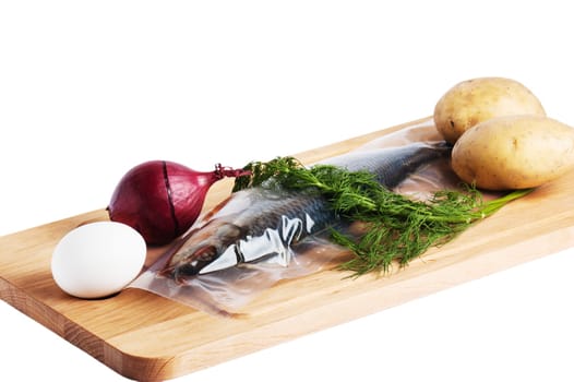Vegetables and a salty herring on a kitchen board