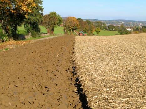 Half-ploughed,brown field in the Kraichgau,Germany. Small green tractor in the background.