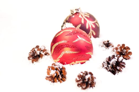 Red baubles and pine cones on snow as a white background
