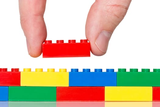 Creativity concept. Hand building up lego wall over a white background.