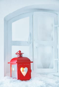 Cheerful red Christmas lantern with a glowing candle standing on a snowy windowsill with copyspace for seasonal greetings