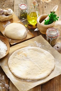 Preparing homemade Italian pizza with a newly rolled dough base surrounded by ingredients for the topping