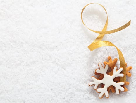 Decorative Christmas biscuit ornament in the form of an iced snowflake with a twirled gold ribbon lying on a bed of fresh white snow with copyspace for your text