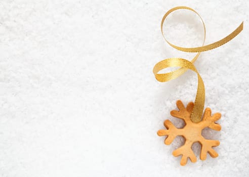 Crisp fresh Christmas snowflake biscuit with a decorative gold ribbon on a background of fresh snow with copyspace for your greetings