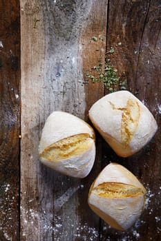 Overhead view of three freshly baked bread rolls lightly dusted with flour on a wooden table top