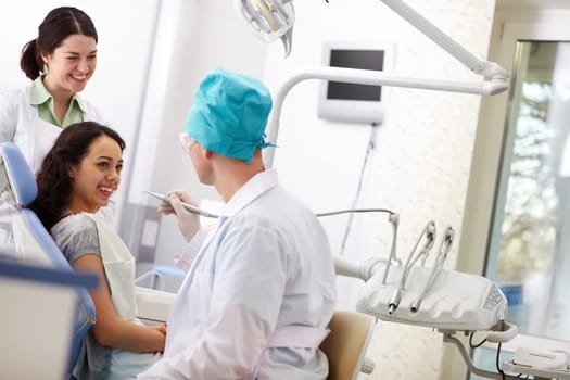Cheerful patient receiving dental care from a friendly doctor and his assistant