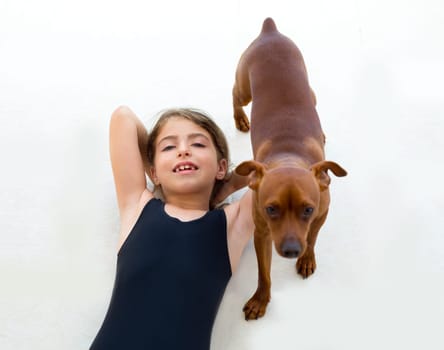Brunette kid girl with summer swimsuit playing with dog lying on floor