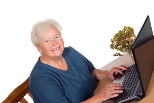 Happy attractive senior lady sitting at her dining table using a laptop computer