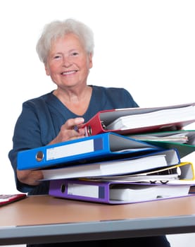 Positive senior woman working part-time in the office to eek out her pension smiling cheerfully from behind a pile of files