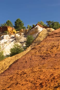 Colorful ocher hills and blue sky in the background. Ocher rocks (French Colorado) near Rustrel (Provence, Southern France)