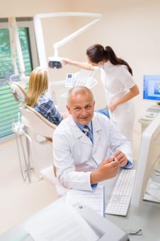 Smiling dental surgeon point model of teeth assistant with patient