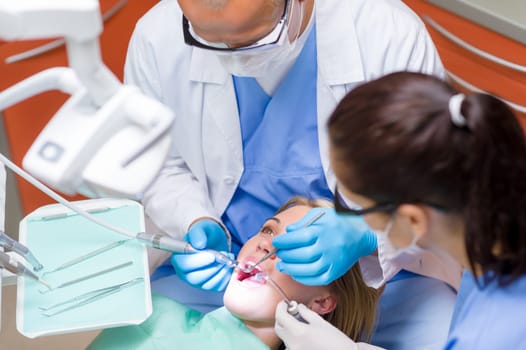Professional dentist and nurse doing dental operation on female patient