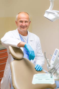 Portrait of mature smiling dentist sitting in modern dental surgery