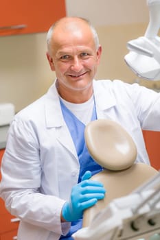 Smiling male dentist sitting behind patient chair modern dental surgery