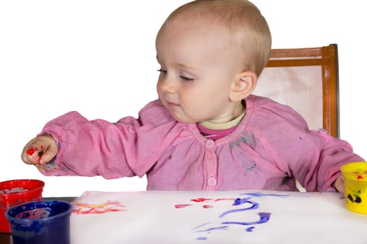 Cute little baby girl experimanting with paint dipping her finger into a jar of pigment to draw on the paper in front of her