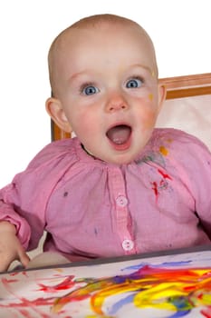 Excited baby girl painter with her eyes and mouth open wide in wonderment at the colourful artwork she has created with a rainbow of colours
