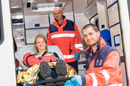 Paramedics helping woman on stretcher in ambulance smiling accident victim