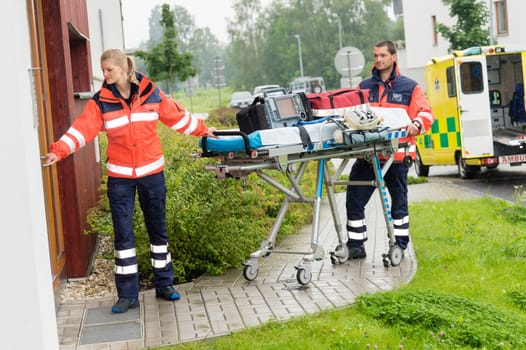 Paramedics carrying emergency stretcher ambulance house call visit door
